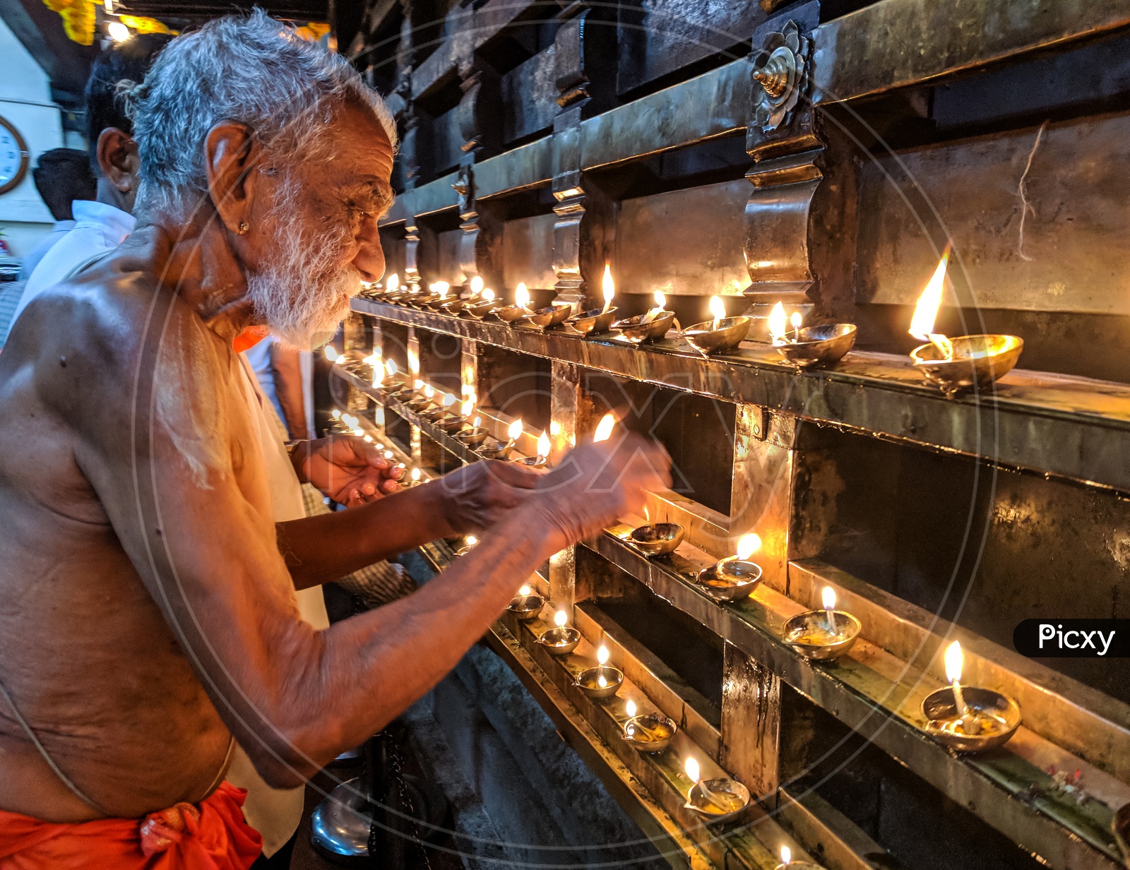 Old Man lighting lamps in a Temple