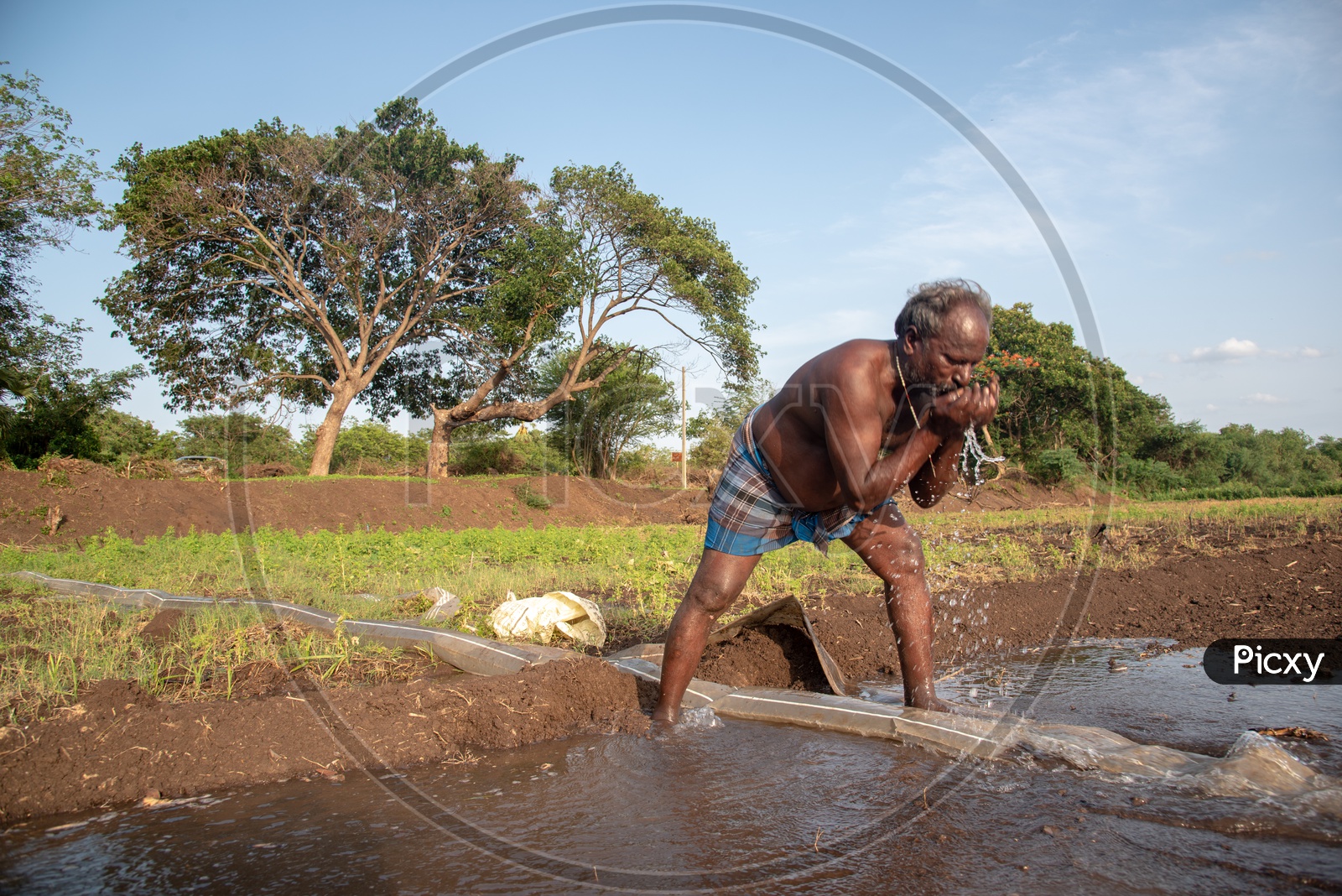 a farmer drinking water from a pumpset in his field