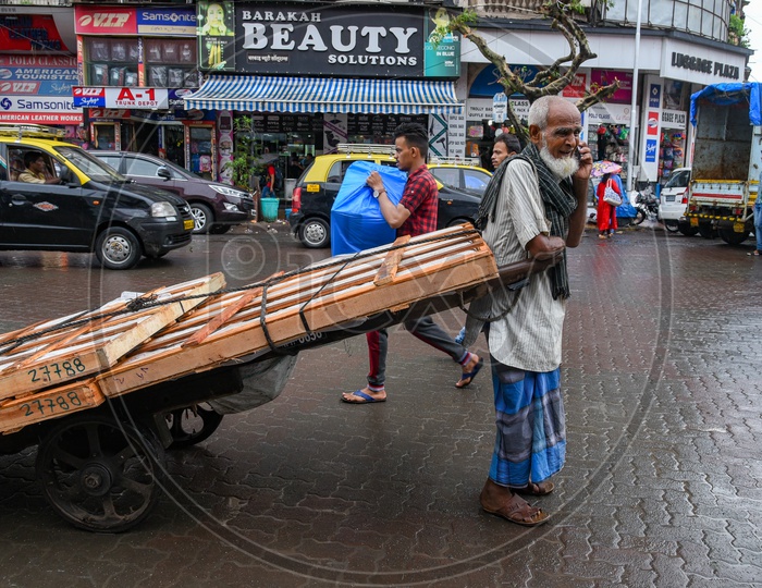 An old man with amputated arm transports heavy goods on hand cart.