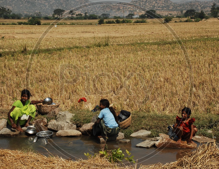 Rural South Indian woman washing dishes in a small stream