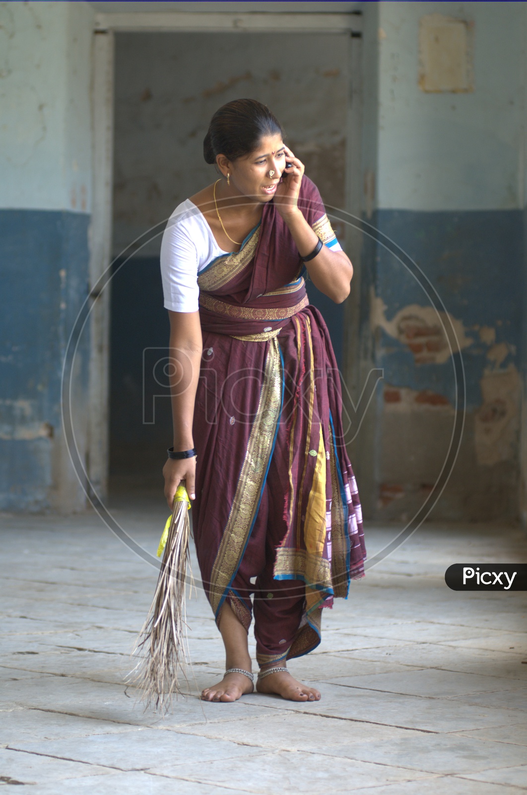 Indian Rural Woman Speaking In Mobile Phone  while Sweeping The Floor