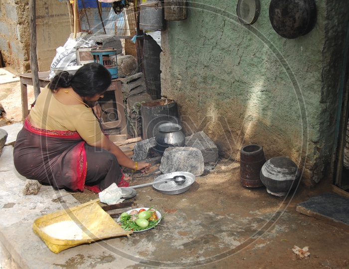 Indian poor woman cooking food infront of a small home