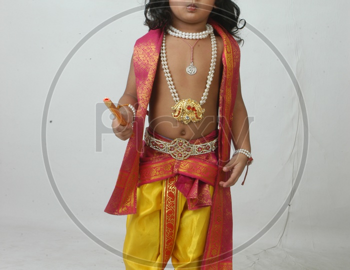 Indian Boy in Lord Sri Krishna Getup  and Eating Chocolate Over an isolated White Background