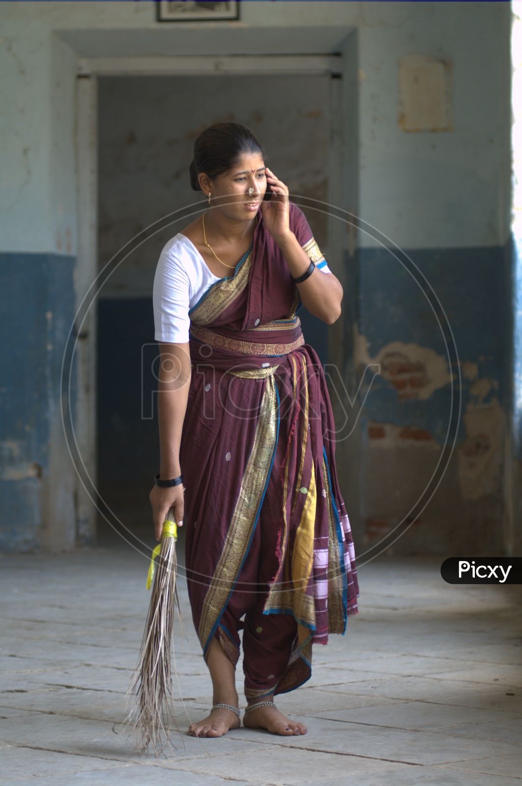 Indian Rural Woman Speaking In Mobile Phone  while Sweeping The Floor