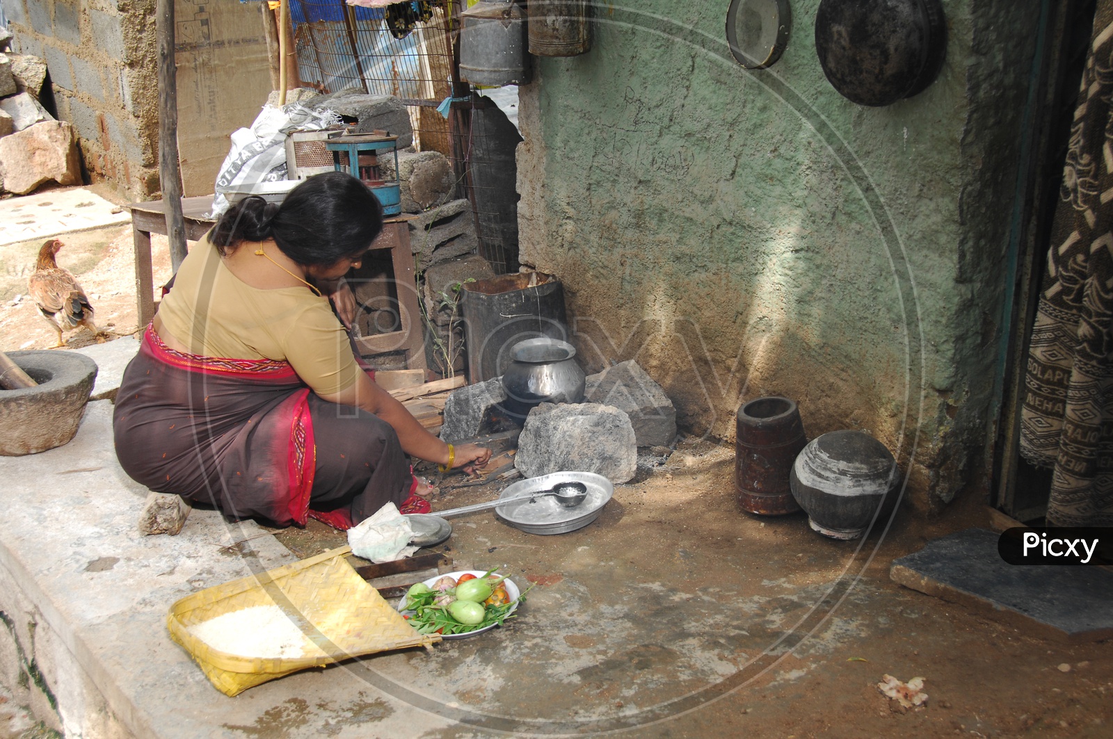 Indian poor woman cooking food infront of a small home