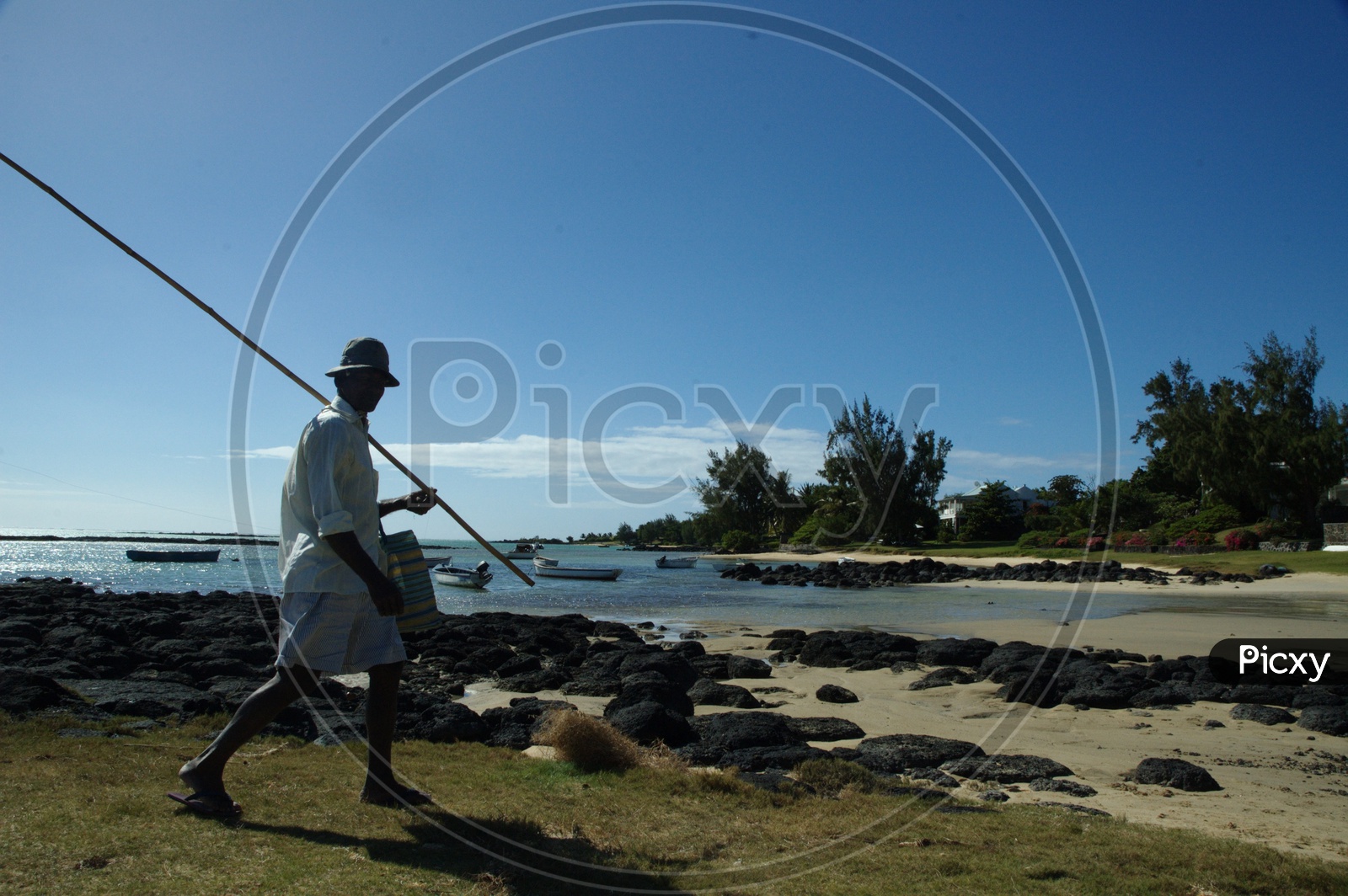 A Man With a Fishing Rod Walking along The Rock Beach