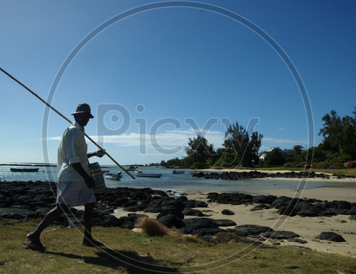 A Man With a Fishing Rod Walking along The Rock Beach