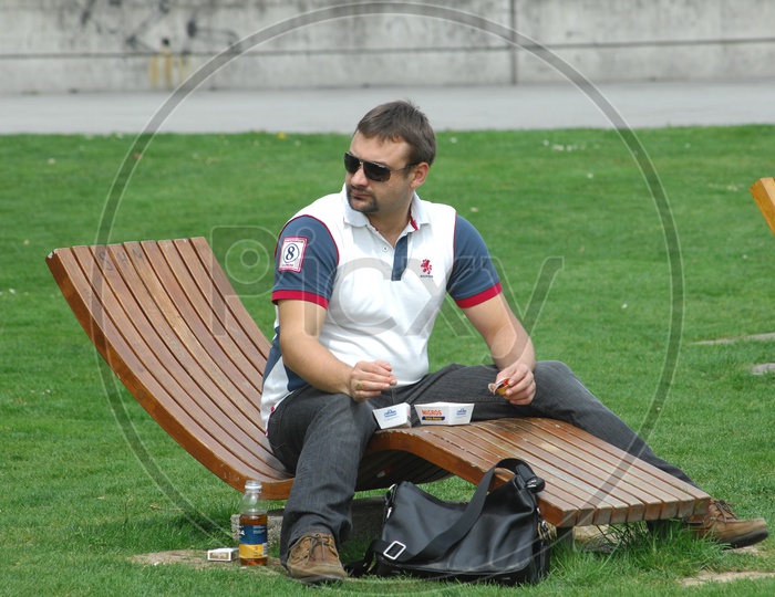 A Man Sitting on a Bench in a Lawn In Europe