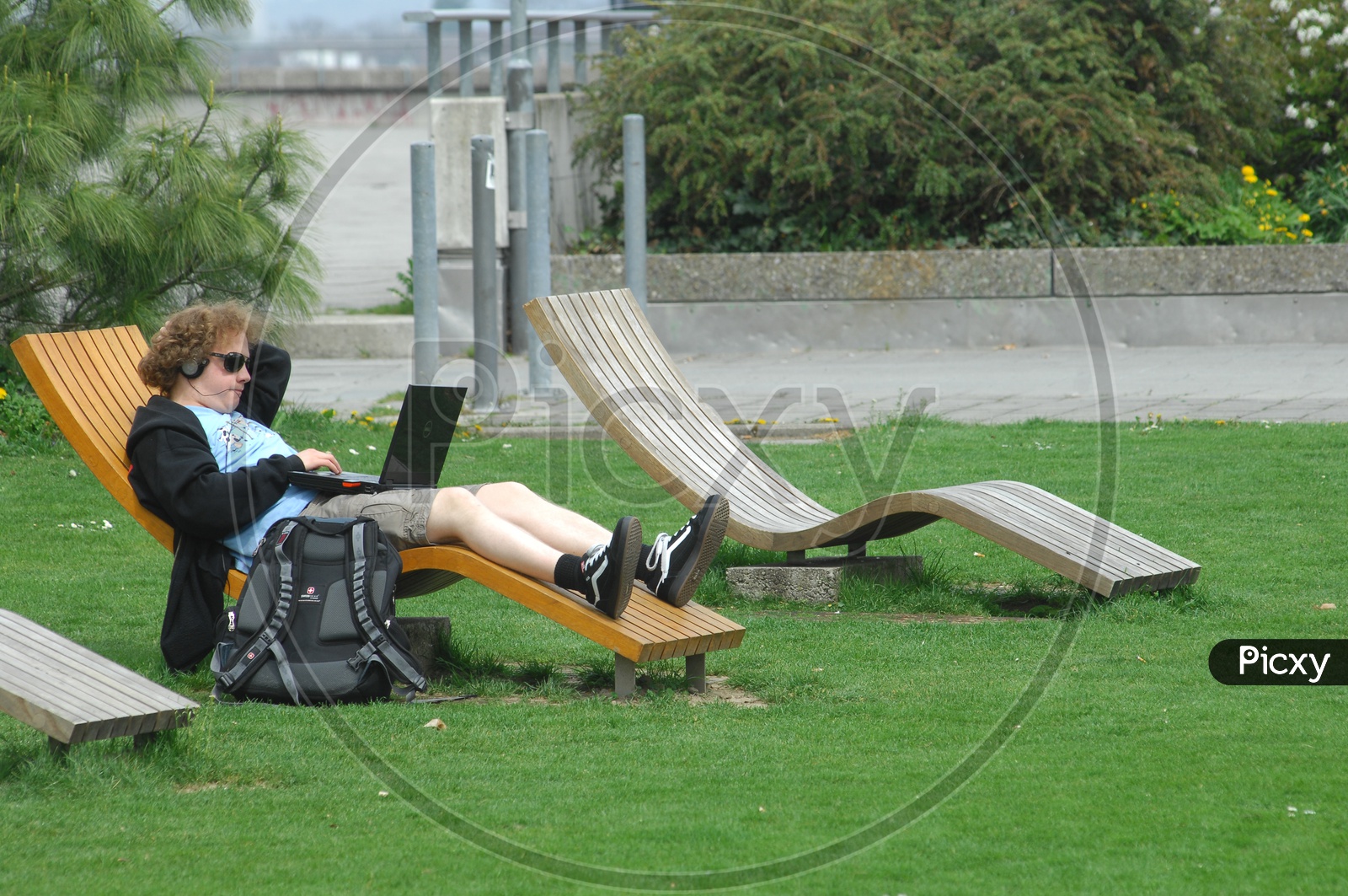 A Man Working In Laptop lying  on a Bench in a Lawn In Europe