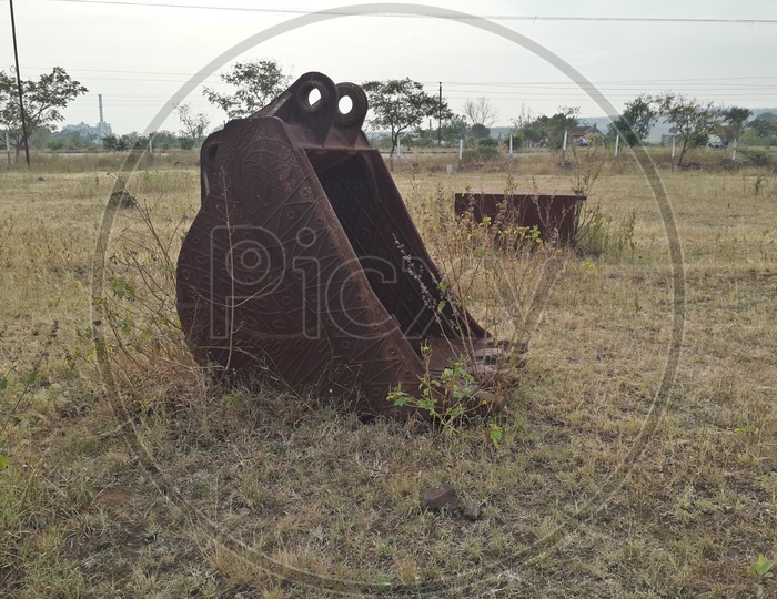 Rusted excavator jaw placed in open grass field