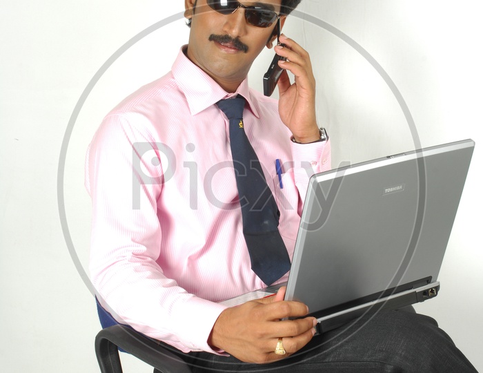 Indian man working and talking over the phone infront of a laptop