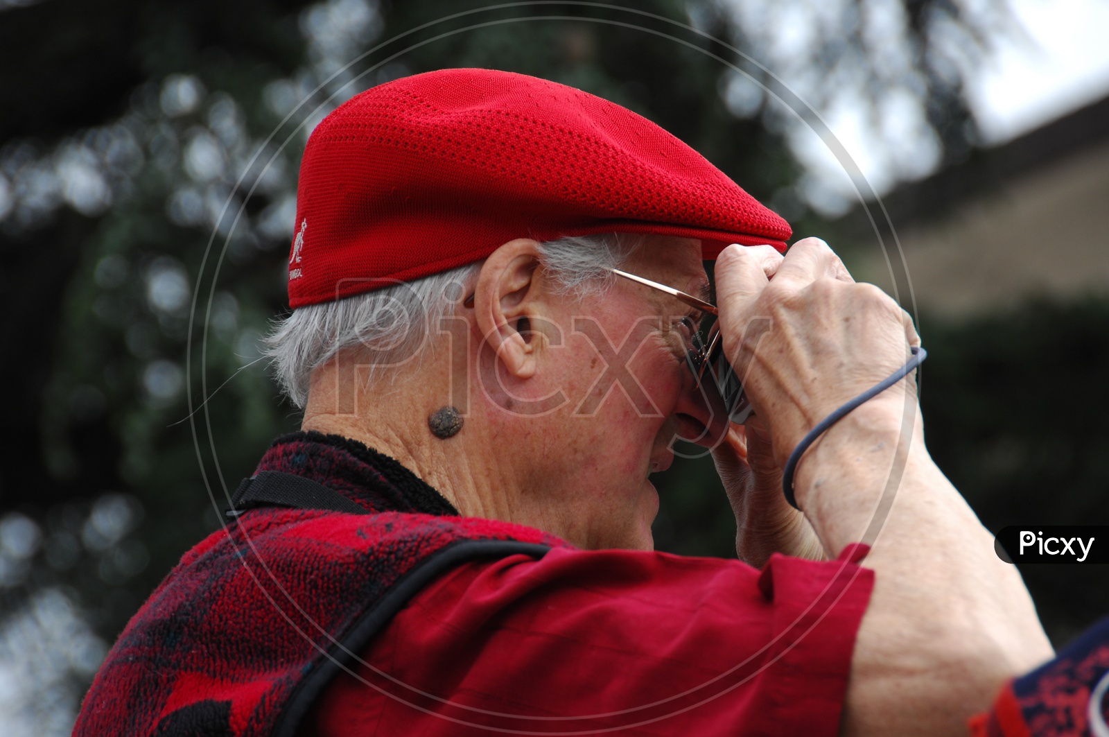 An old man wearing a red cap clicking a picture