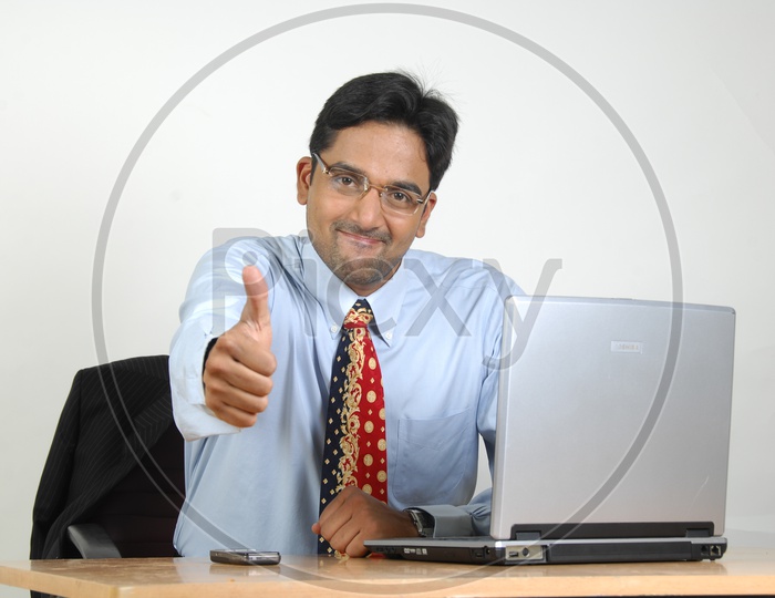 Indian Office Employee With Old Laptop And Thumbsup Gesture At Office Desk