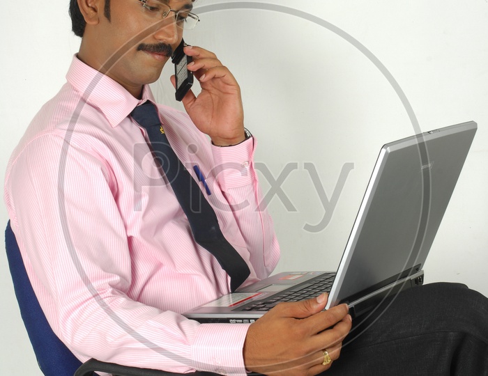 Indian man working and talking over the phone infront of a laptop