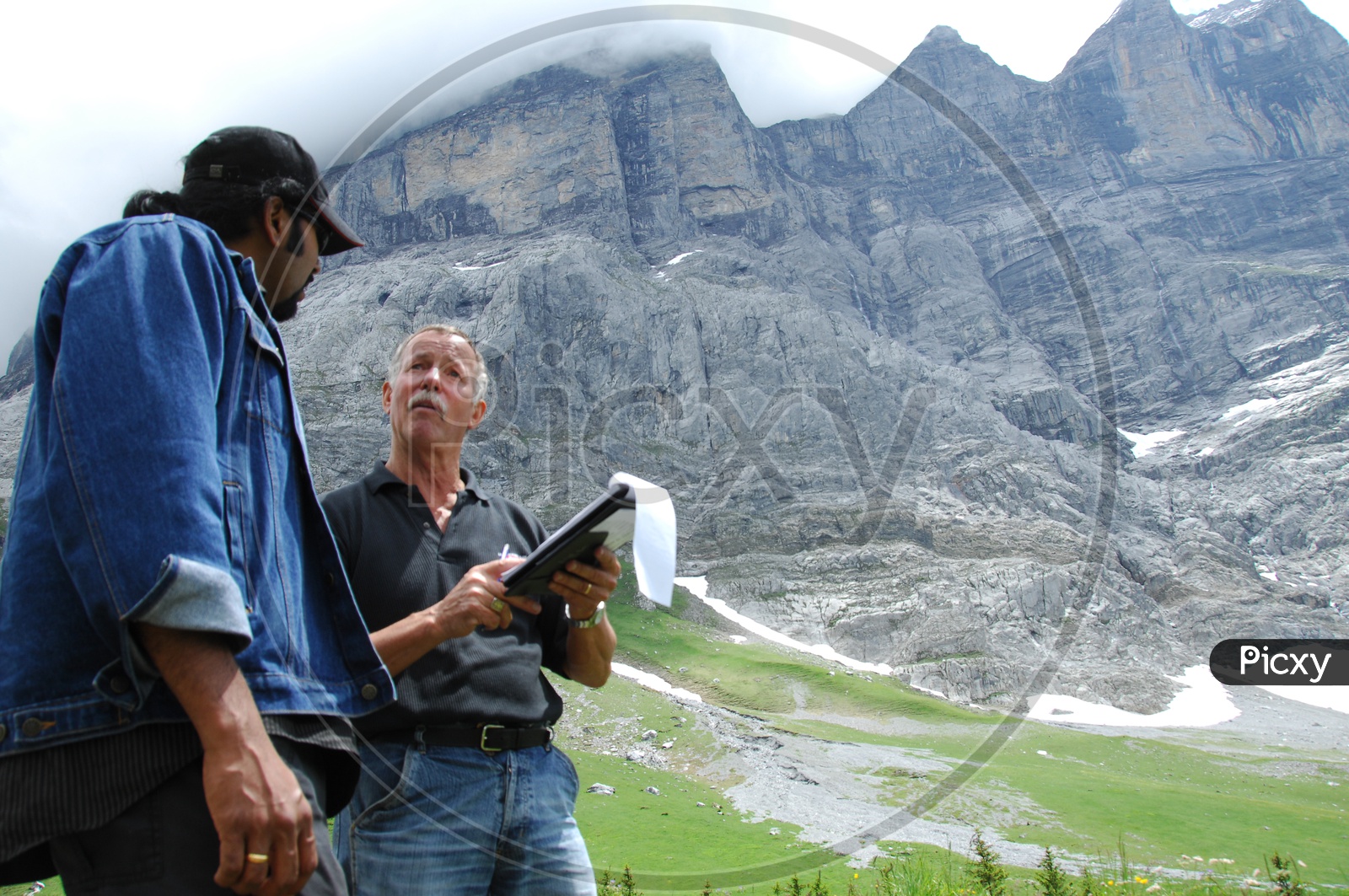 Image of Two men talking near a mountain area, clouds seen at a far ...