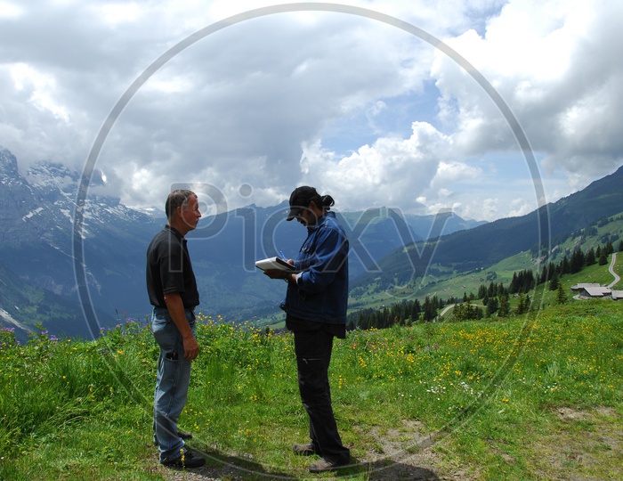 Image of Two men talking near a mountain area, clouds seen at a far ...
