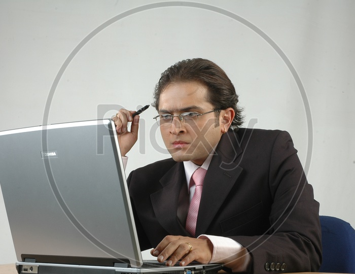 Indian man working and thinking infront of a laptop