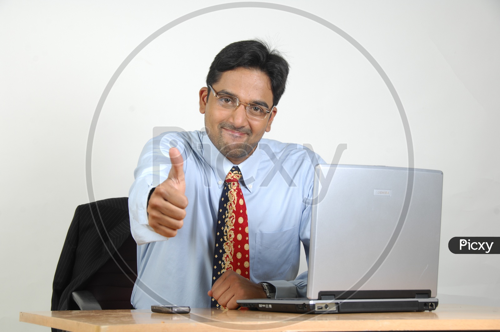 Indian Office Employee With Old Laptop And Thumbsup Gesture At Office Desk