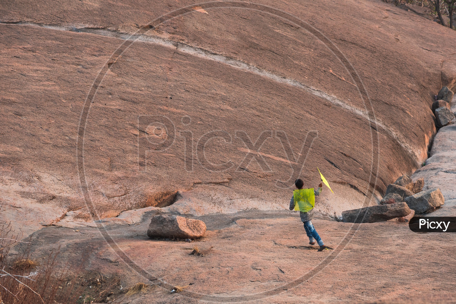 A Small Kid Playing with a Kite On a Rock Hill