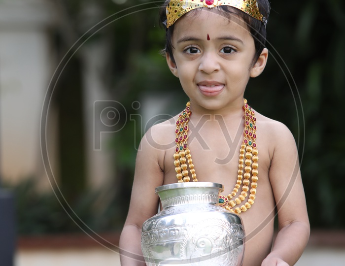 Little boy dressed up as Lord Krishna holding  silver items