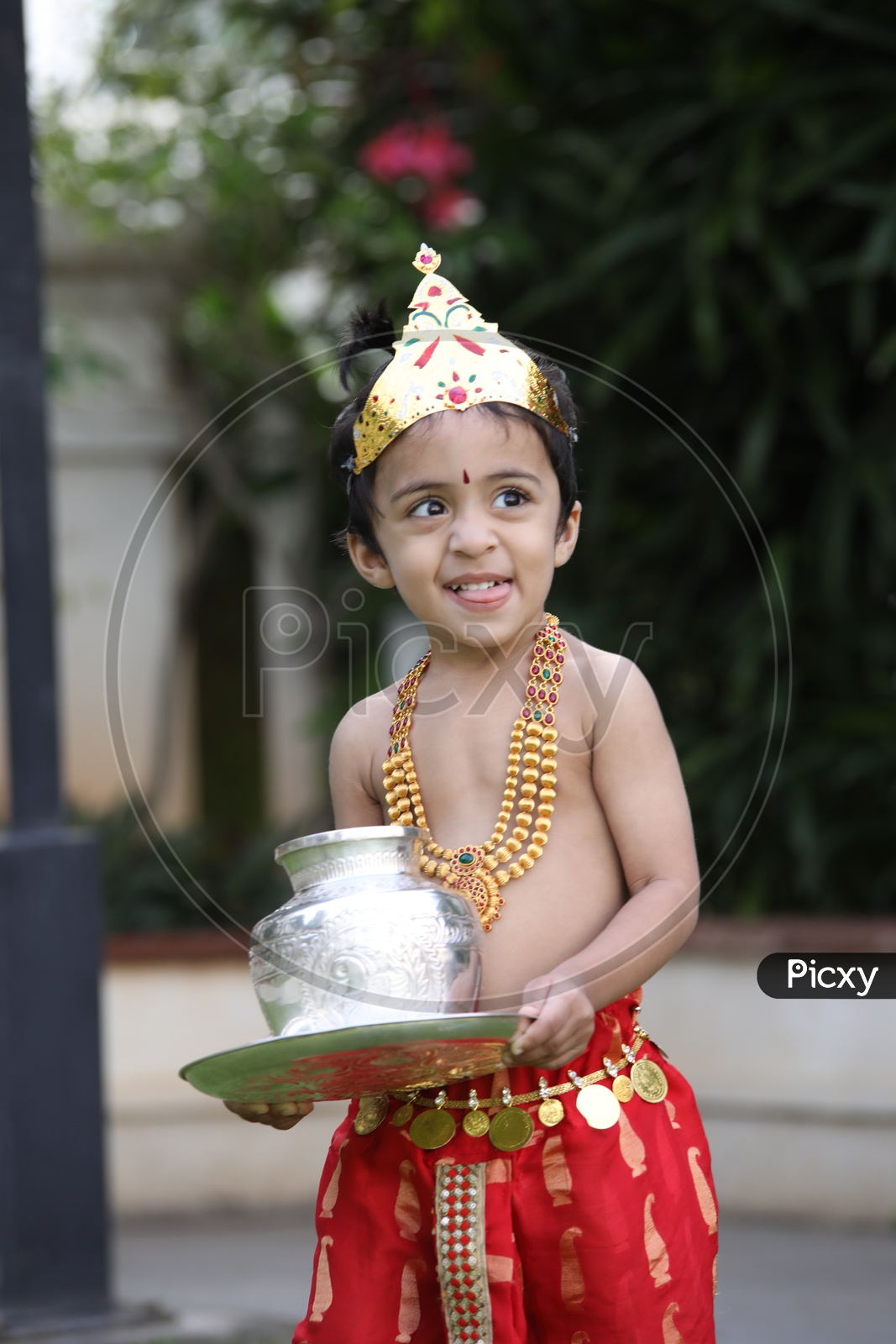 Little boy dressed up as Lord Krishna holding  silver items