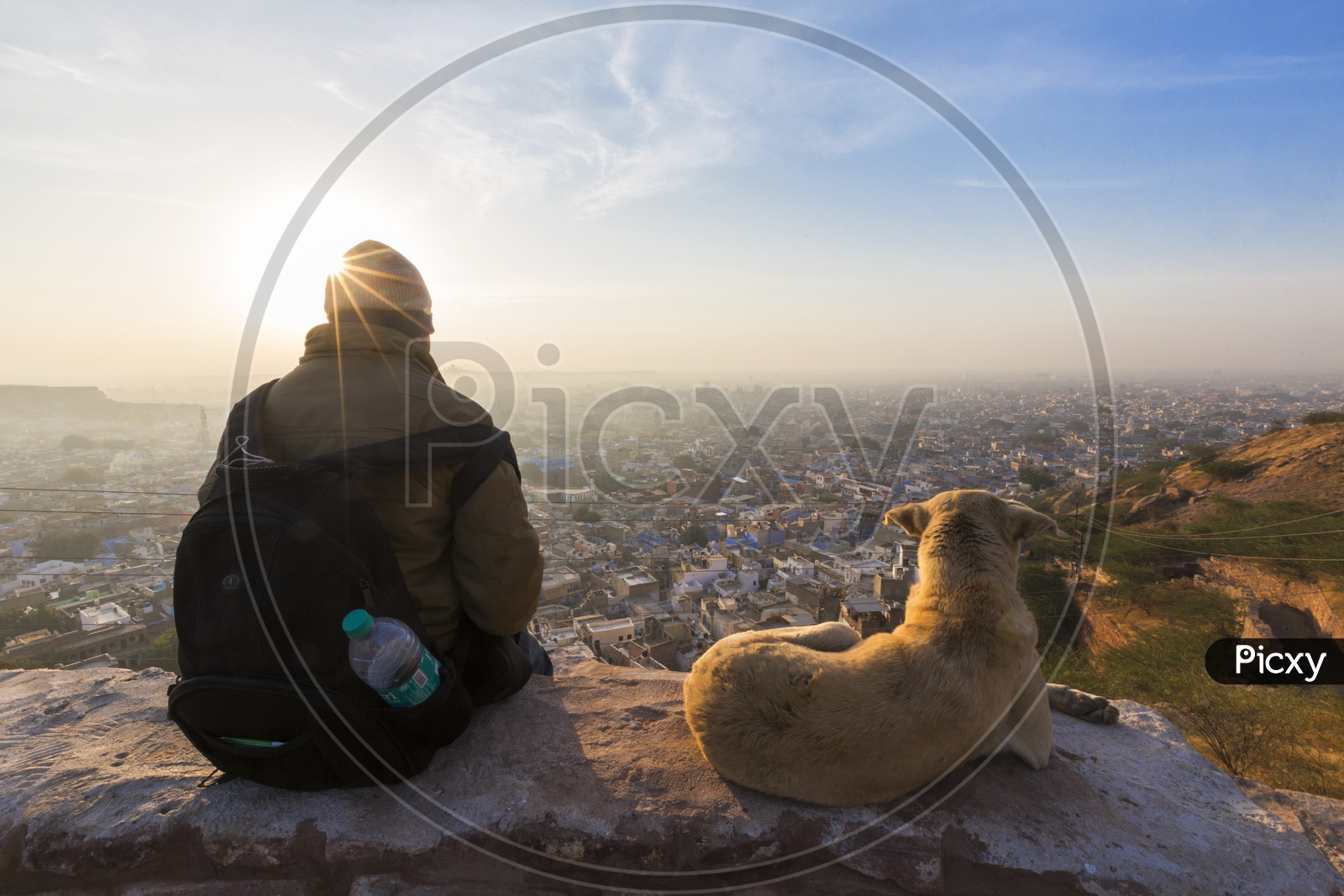 An Indian Man Sitting on a View Point In Mehrangarh Fort and Watching The Sunset Over The Jodhpur City witha Dog Besides Him