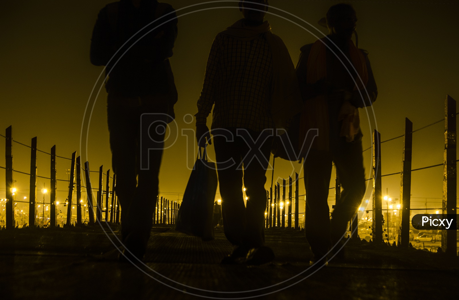 Three men walking towards a fence road during the night