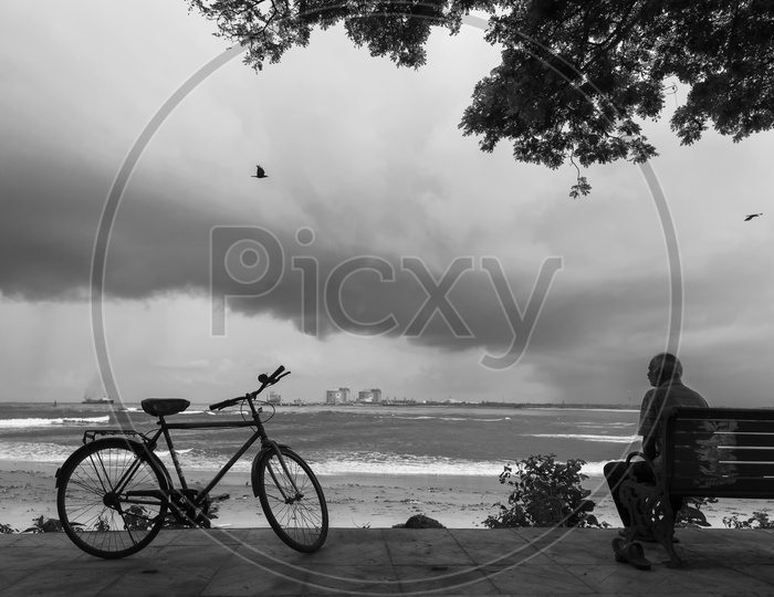 An Old Man Sitting alone On a Bench in Sea Shore with his Cycle besides Him In Kerala