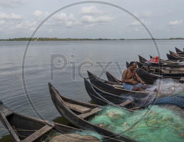 A kerala Fisherman Repairing His Fishing net sitting on boats