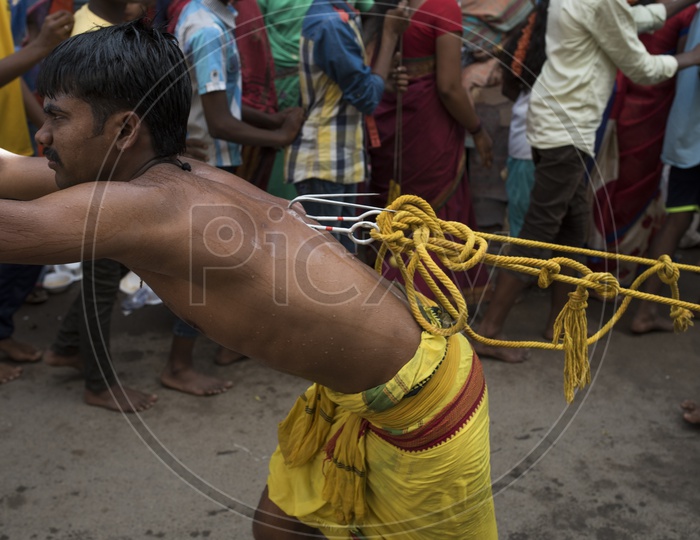 A Man Pulliing a Vehicle By Piercing his body With an iron hook as a coustom in dussera celebrations