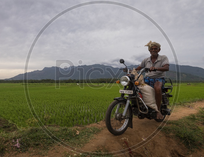 A Farmer Riding a Moped With a Smile in Paddy Fields