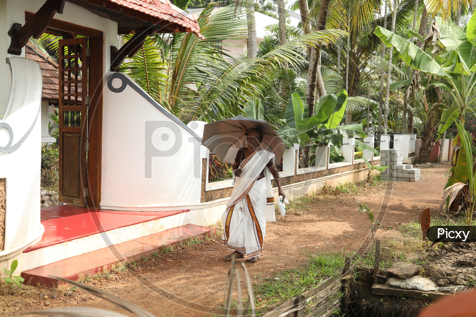 Old keralite woman walking with an umbrella along the road