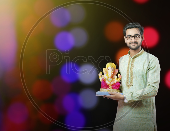 Indian Young Man In Traditional Attire  With Lord Ganesh Idol On An Isolated Bokeh Background