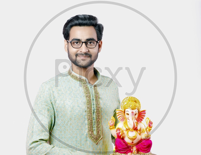 Indian Young Man In Traditional Attire  With Lord Ganesh Idol On An Isolated Background