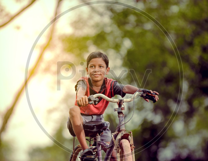 Indian Boy Child Riding Bicycle in Rural India with a Smiling Face And Looking To Camera