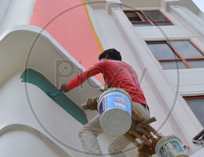 A Painting Worker Painting A Building By The Hanging With The Help of a Rope