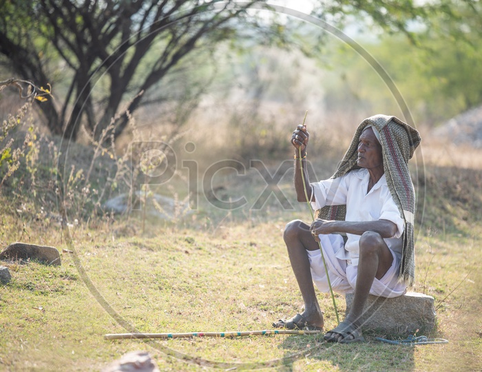 An Old Man In Indian Village Sitting in  His Agricultural Land and Smoking