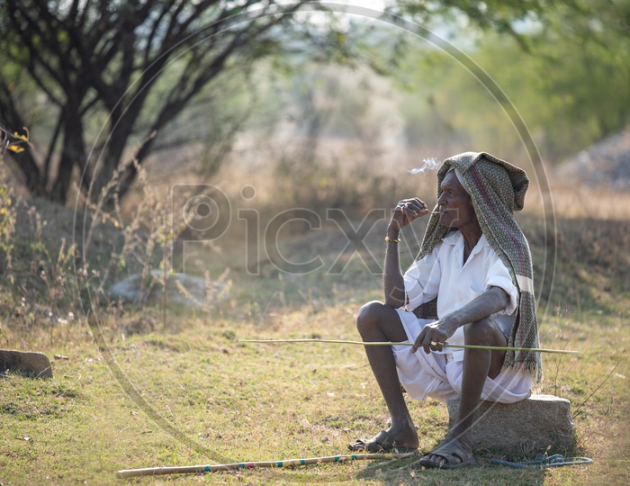 An Old Man In Indian Village Sitting in  His Agricultural Land and Smoking