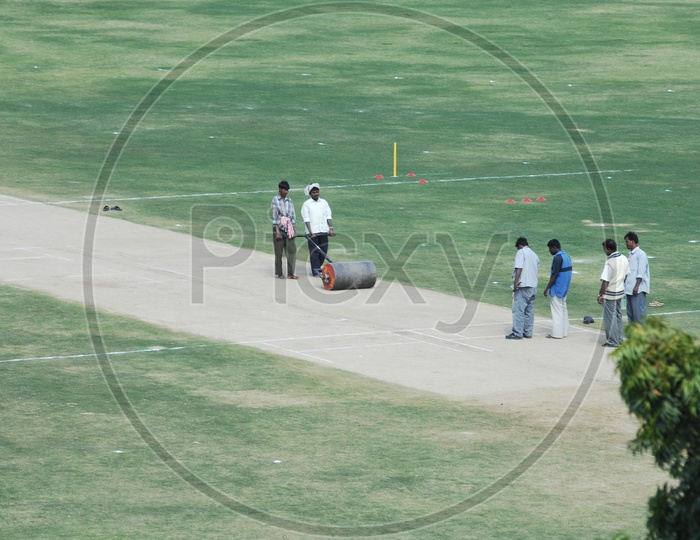 Indian Man  Working on a Cricket Pitch With a Roller