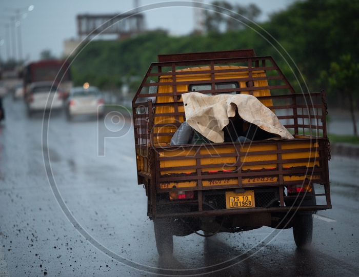 People Taking Cover With a Plastic Sheet While Travelling In a Truck Auto From  Heavy Rain On National Highway