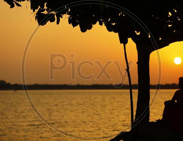 Silhouette of an Young Indian Girl Sitting At Godavari river  Bank  With Sunset Sky In Background