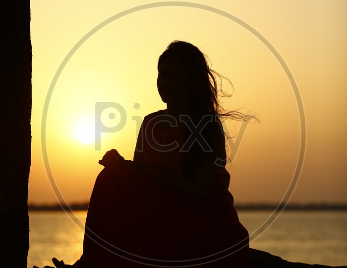 Silhouette of an Young Indian Girl Sitting At Godavari river  Bank  With Sunset Sky In Background