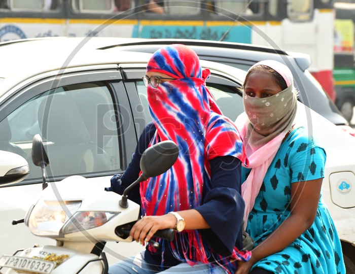 Indian women riding scooty with their faces covered with scarfs