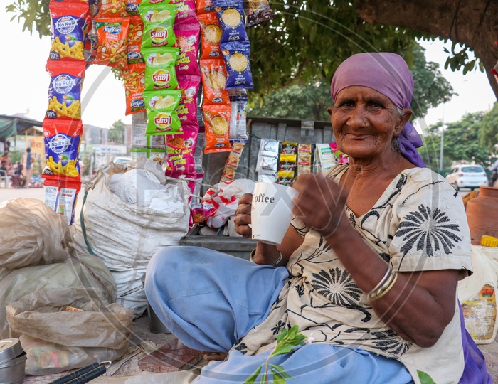 An Old Woman Having Tea In a Cup At a Road Side vendor Stall