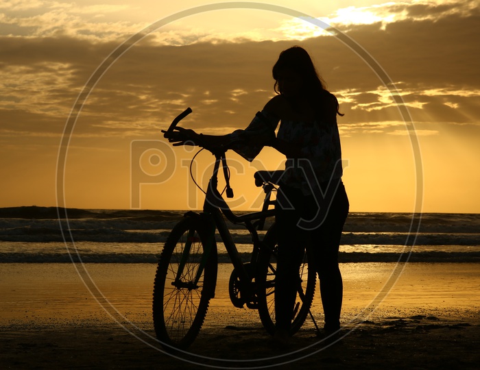 Silhouette Of a Young Girl With Bicycle In a Beach With Golden Sky In Background