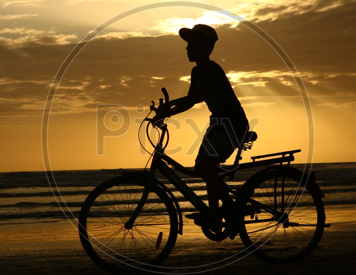 Young Boy Riding Bicycle Over a Golden Sunset Sky In Background At a Beach in Goa