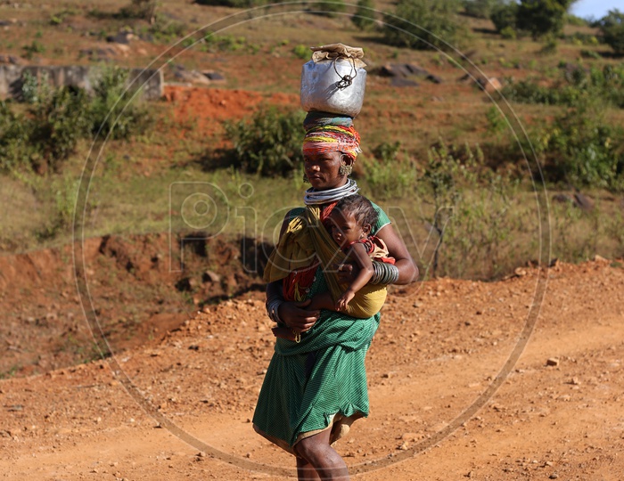 Bonda Tribal Woman Carrying Water Vessel And Her Child And Walking along Tribal Village Roads