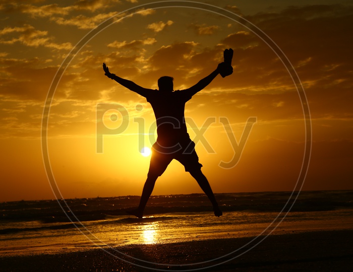 Silhouette Of a Photographer Jumping In Joy With DSLR At a Beach With Sunset Golden Sky In Goa