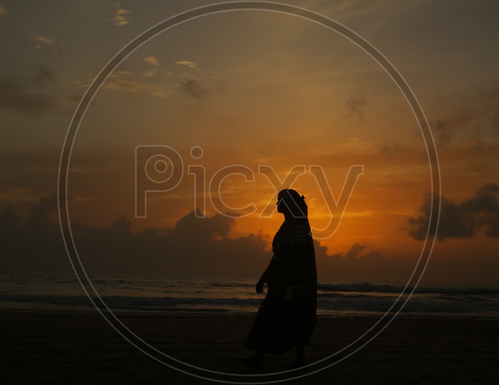 Silhouette Of a Woman Standing In a beach Alone With Sunset Sky In Background