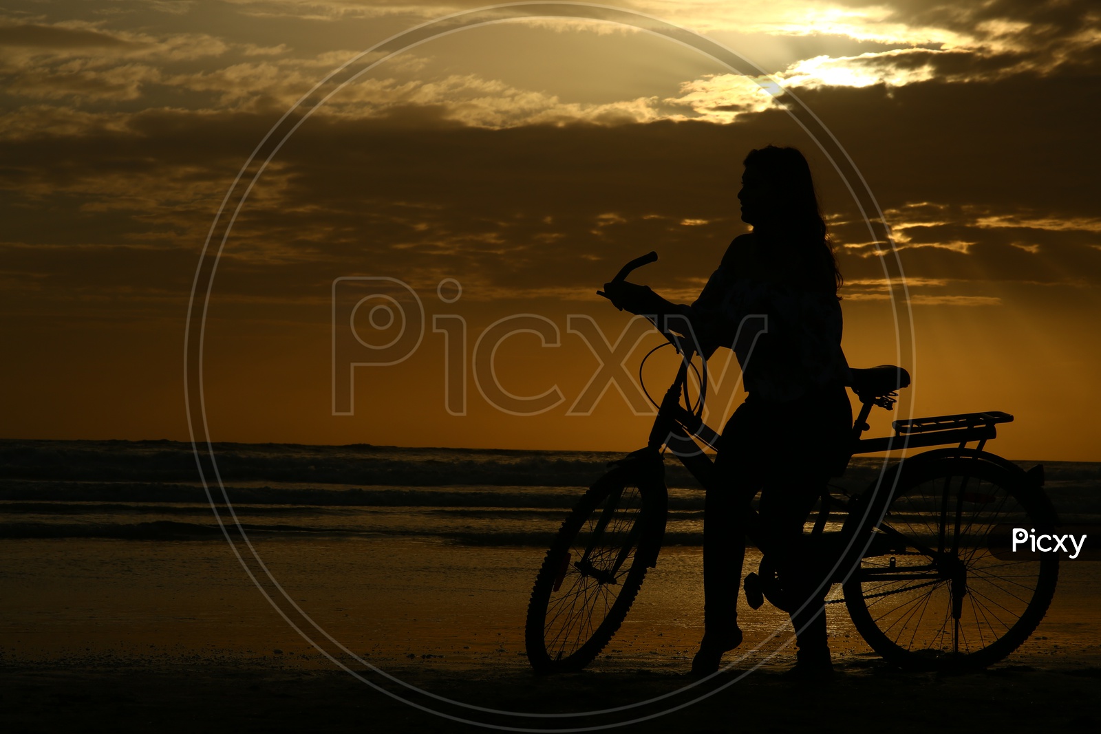 Silhouette Of a Young Girl With Bicycle In a Beach With Golden Sky In Background